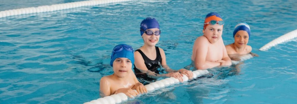 A group of boys and girls train and learn to swim in the pool with an instructor. Development of children's sports.